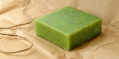 Green handmade herbal soap bar on a brown wrapping paper. Natural toiletries and hygiene products with herbs and essential oils. Front view.